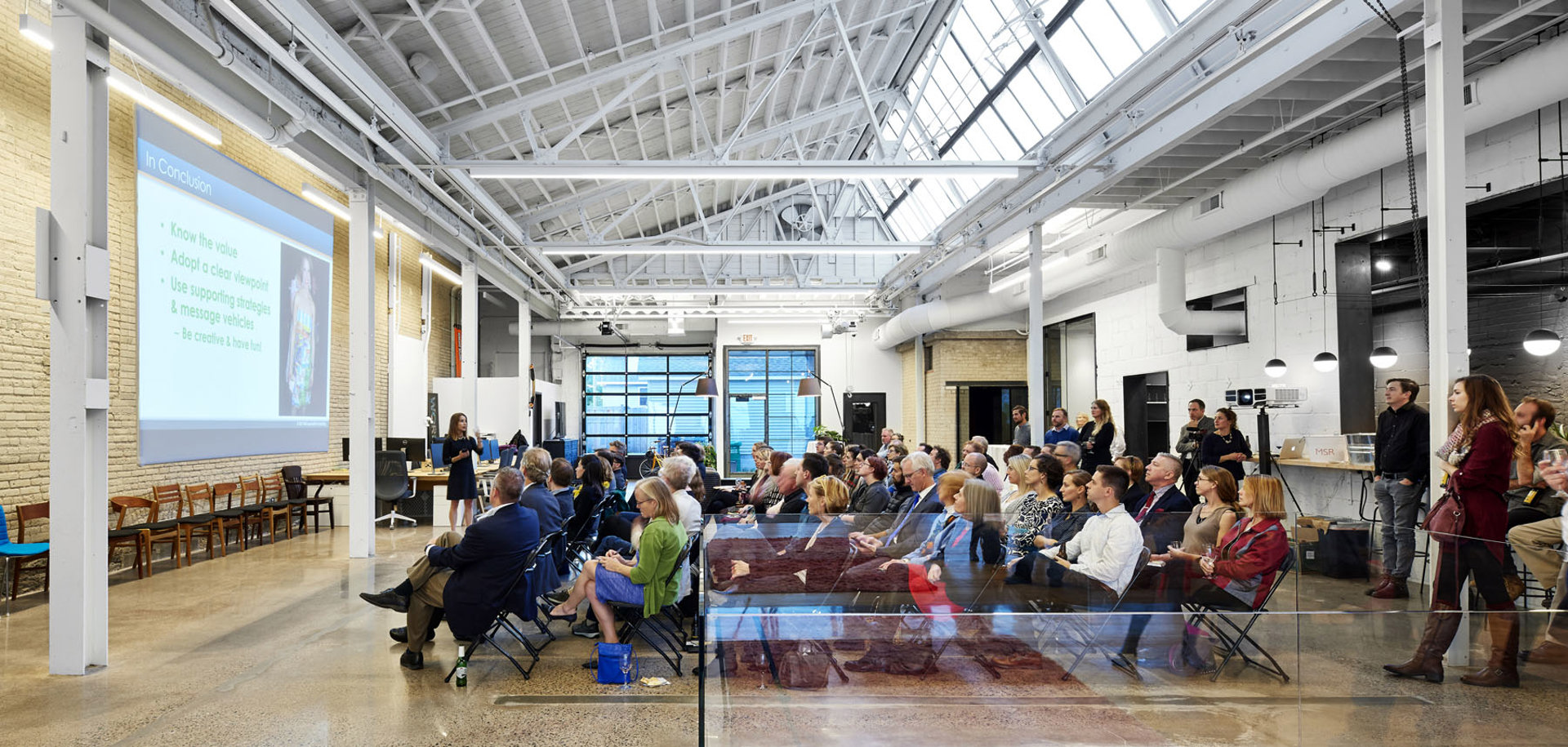 A group of people seated in a large room listening to a presentation.