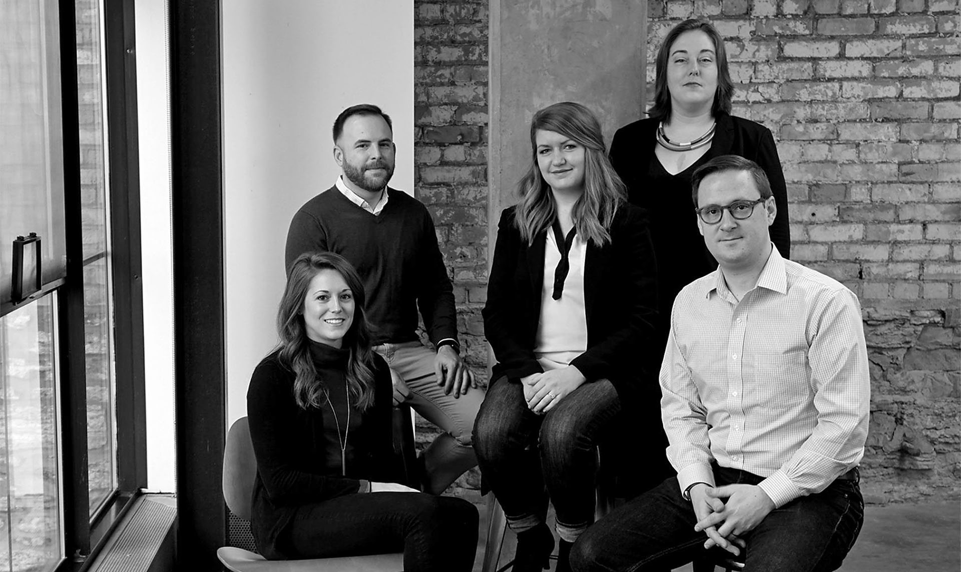A black and white photo of a group of five people posing together in an office