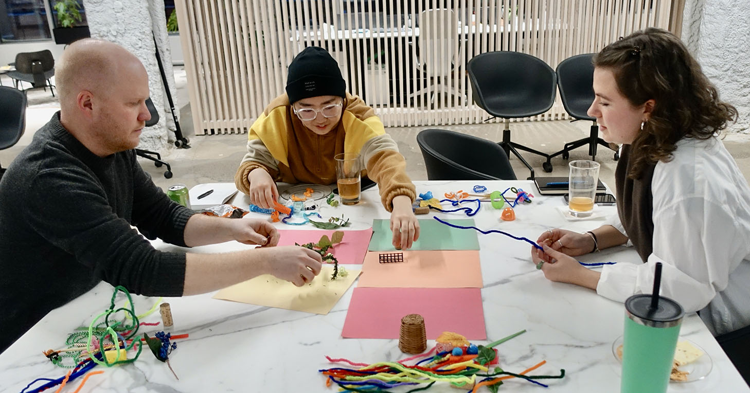 Three people at a table working together using craft materials like pipe cleaners and colored paper