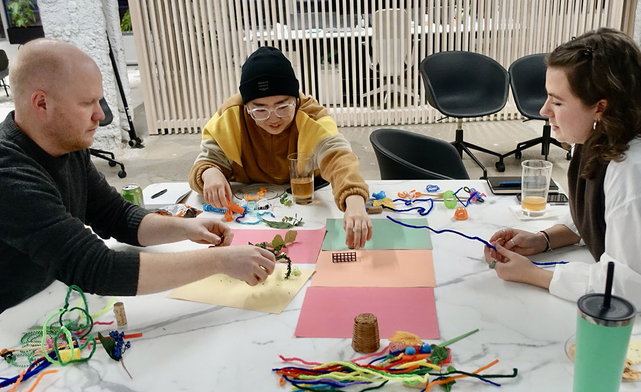 Three people at a table working together using craft materials like pipe cleaners and colored paper